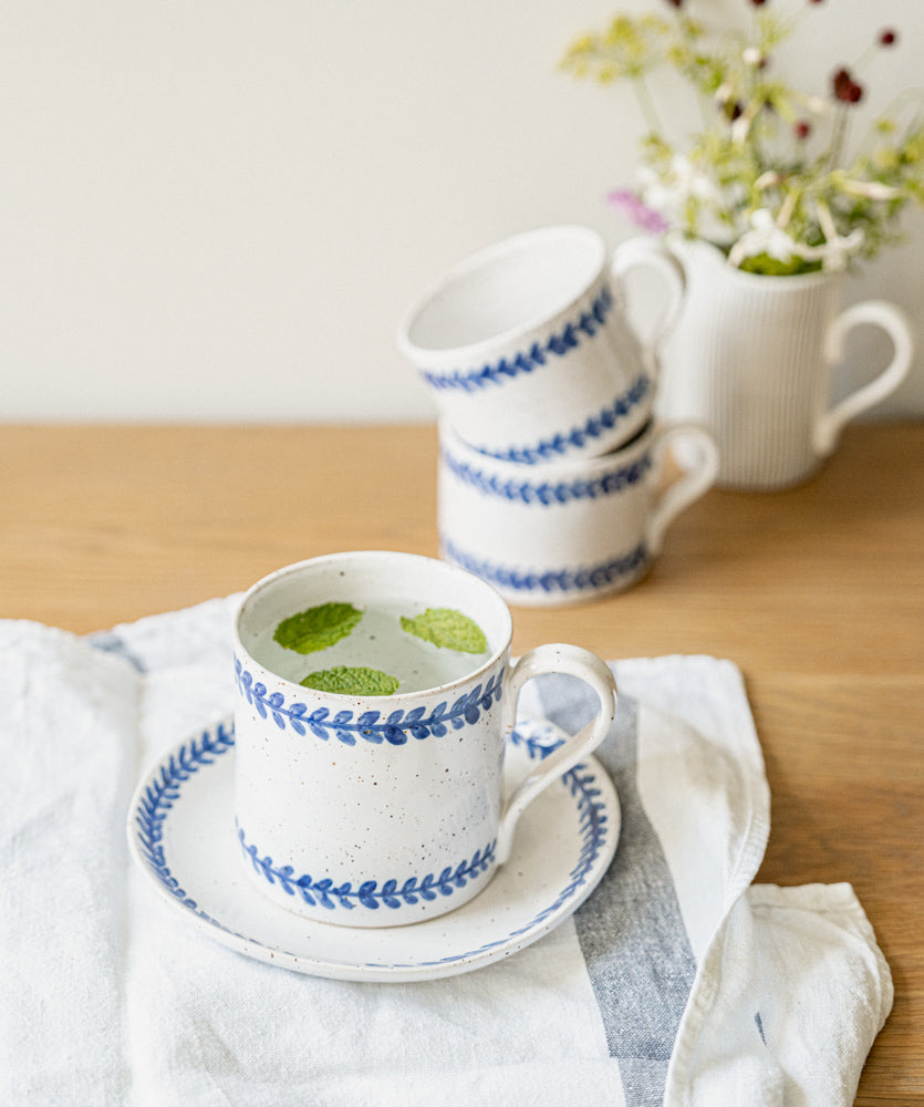 Handmade stoneware mug with hand-painted cobalt blue leaf border on a white glaze.