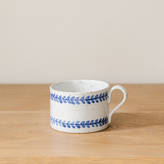 Handmade stoneware coffee cup with a hand-painted cobalt blue leaf border and glossy white glaze